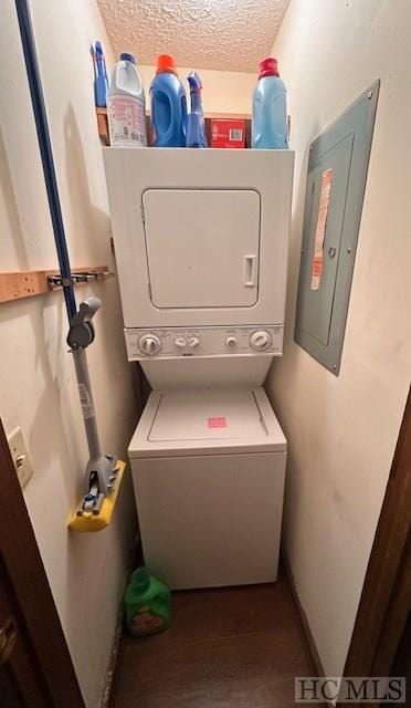 clothes washing area featuring stacked washer / dryer, electric panel, and a textured ceiling