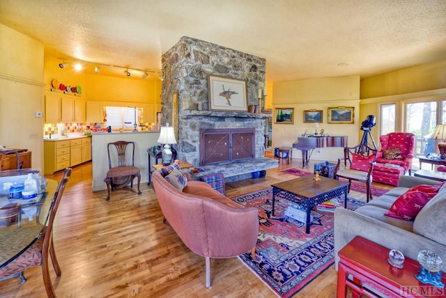 living room featuring track lighting, wood-type flooring, a stone fireplace, and a textured ceiling