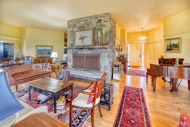 living area featuring a stone fireplace, an inviting chandelier, and light hardwood / wood-style floors