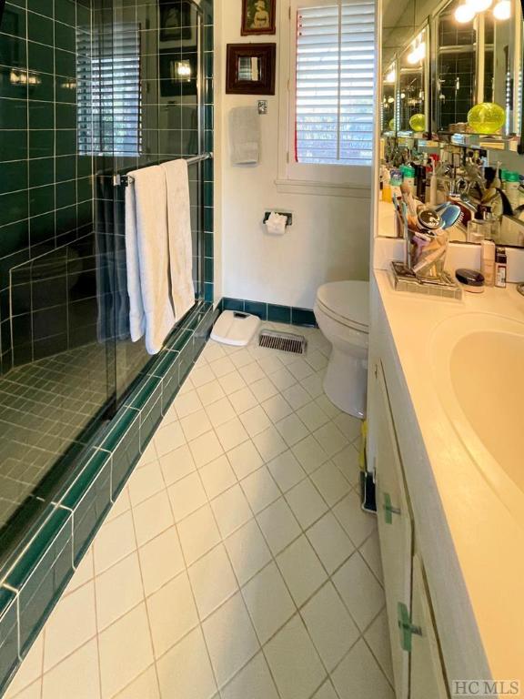 bathroom with toilet, vanity, a shower with door, and tile patterned flooring