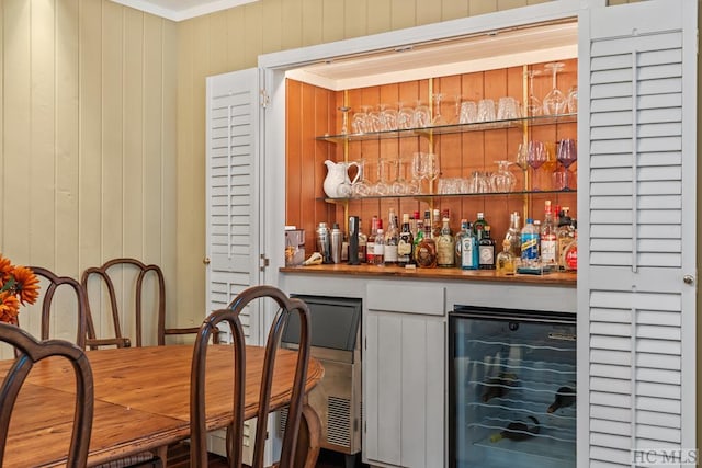 bar with crown molding, wood walls, and wine cooler