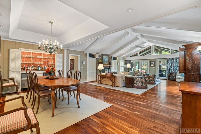 dining room featuring hardwood / wood-style floors, vaulted ceiling with beams, ceiling fan with notable chandelier, and a raised ceiling