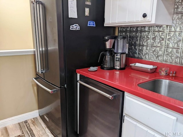 kitchen with hardwood / wood-style floors, tasteful backsplash, white cabinetry, sink, and stainless steel dishwasher