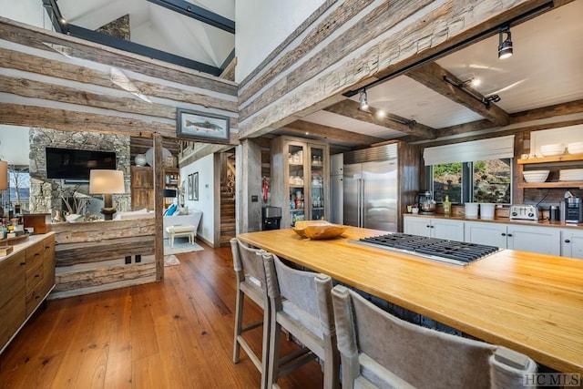 kitchen with hardwood / wood-style flooring, appliances with stainless steel finishes, white cabinets, beamed ceiling, and a high ceiling