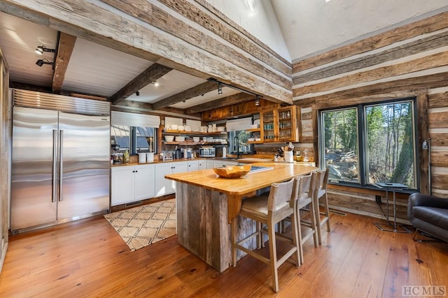 kitchen with appliances with stainless steel finishes, beamed ceiling, butcher block counters, white cabinets, and light hardwood / wood-style flooring