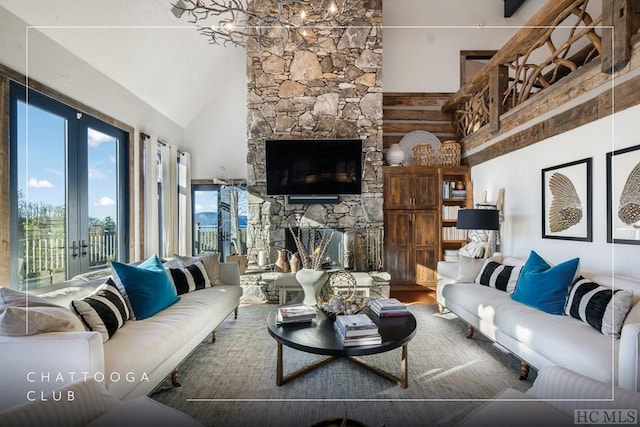 living room featuring hardwood / wood-style flooring, a stone fireplace, an inviting chandelier, and french doors