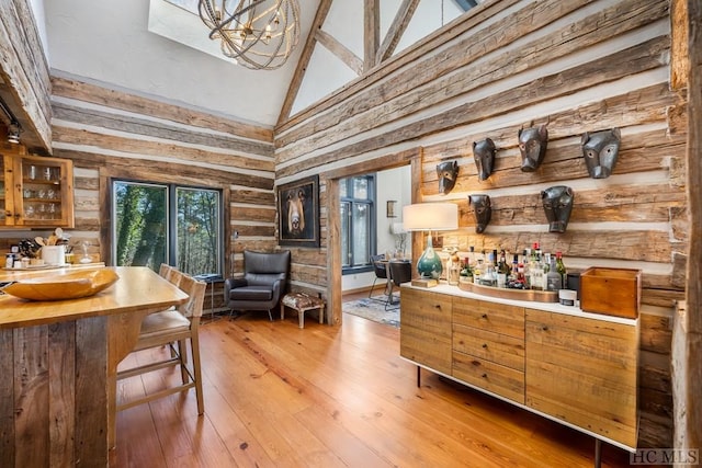 bar featuring high vaulted ceiling, light hardwood / wood-style flooring, a notable chandelier, and log walls