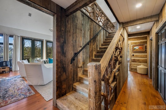 stairs with hardwood / wood-style flooring, wooden walls, beamed ceiling, and french doors