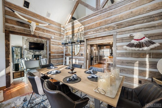 dining space featuring a stone fireplace, hardwood / wood-style floors, rustic walls, and high vaulted ceiling