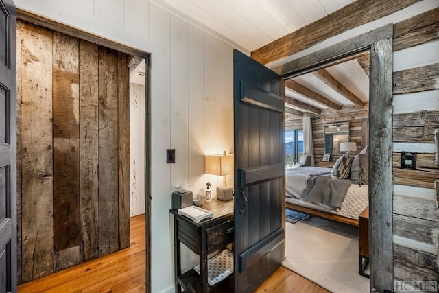 bedroom with light hardwood / wood-style flooring, wooden walls, and beam ceiling