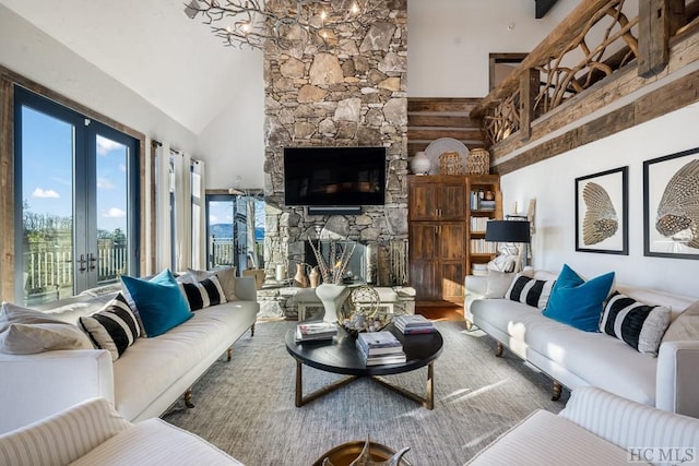 living room with a stone fireplace, a towering ceiling, wood-type flooring, a notable chandelier, and french doors