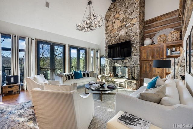 living room featuring high vaulted ceiling, a notable chandelier, a fireplace, wood-type flooring, and french doors