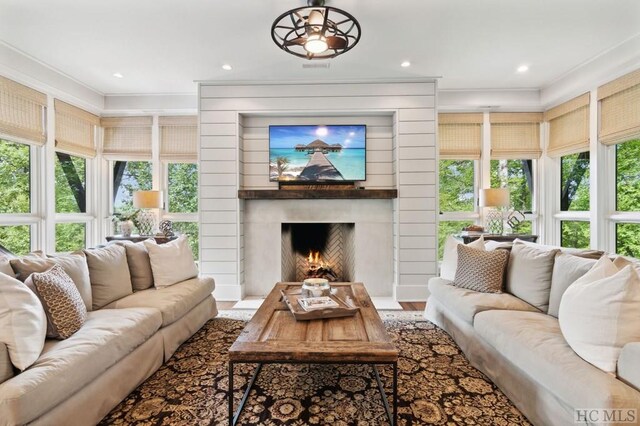 living room featuring a healthy amount of sunlight, wood-type flooring, a fireplace, and ornamental molding