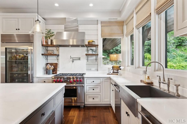 kitchen featuring pendant lighting, wall chimney range hood, sink, white cabinetry, and premium appliances