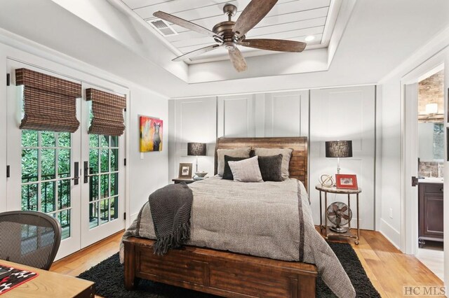 bedroom featuring connected bathroom, light wood-type flooring, a tray ceiling, ceiling fan, and access to exterior