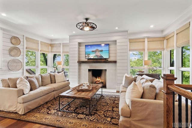 living room featuring hardwood / wood-style flooring, ornamental molding, a large fireplace, and a healthy amount of sunlight