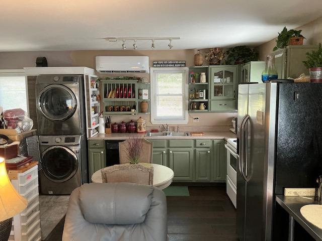 kitchen featuring stainless steel appliances, stacked washer and clothes dryer, green cabinetry, a wall mounted air conditioner, and a sink