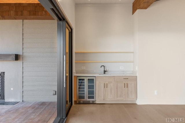 bar featuring sink, wine cooler, light hardwood / wood-style floors, beamed ceiling, and light brown cabinets