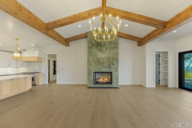 unfurnished living room with an inviting chandelier, vaulted ceiling with beams, a tiled fireplace, and light wood-type flooring