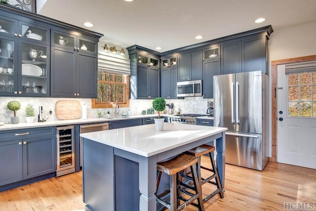 kitchen with wine cooler, sink, appliances with stainless steel finishes, a kitchen island, and light hardwood / wood-style floors