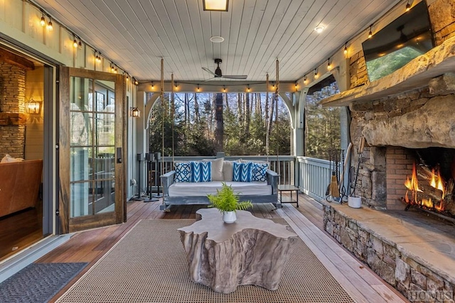 sunroom featuring an outdoor stone fireplace, wooden ceiling, and ceiling fan