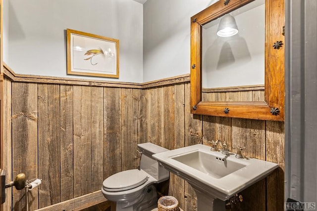 bathroom with sink, wooden walls, and toilet