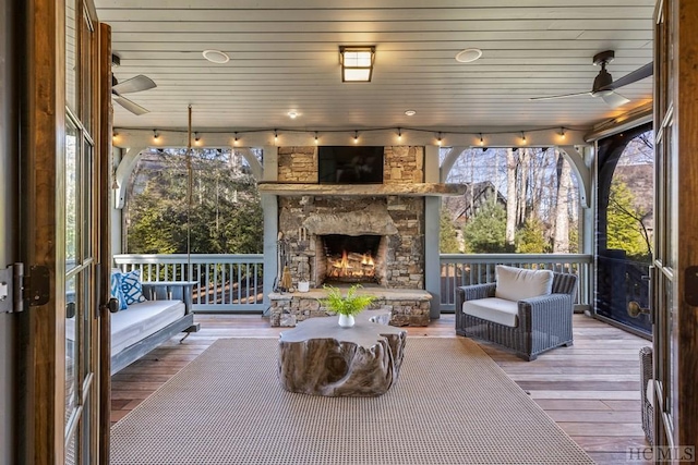 sunroom with wood ceiling, ceiling fan, a healthy amount of sunlight, and an outdoor stone fireplace