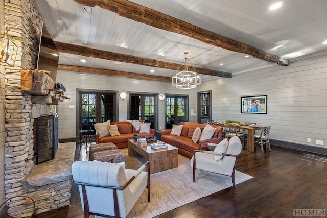 living room with dark wood-type flooring, beam ceiling, a notable chandelier, a stone fireplace, and wood walls