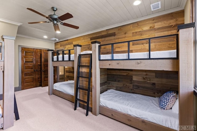 carpeted bedroom with ornamental molding, a closet, ceiling fan, and wood walls