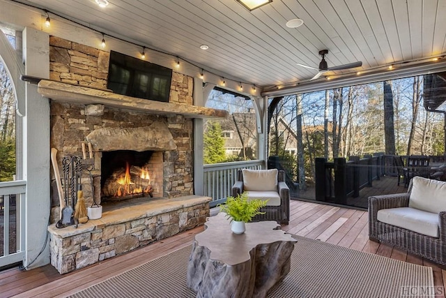 sunroom with ceiling fan, a wealth of natural light, wooden ceiling, and an outdoor stone fireplace