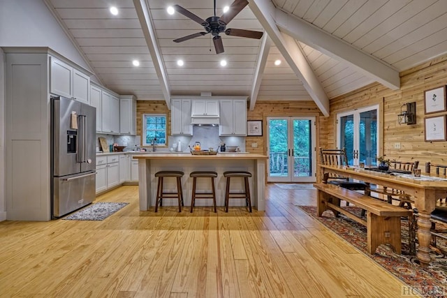 kitchen featuring under cabinet range hood, lofted ceiling with beams, light countertops, a kitchen breakfast bar, and stainless steel refrigerator with ice dispenser