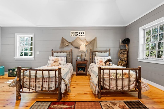 bedroom with vaulted ceiling, multiple windows, and wood-type flooring