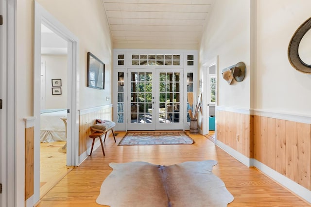 entrance foyer featuring wooden walls, vaulted ceiling, wainscoting, french doors, and wood finished floors