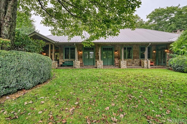 back of property with metal roof, stone siding, a lawn, and a porch