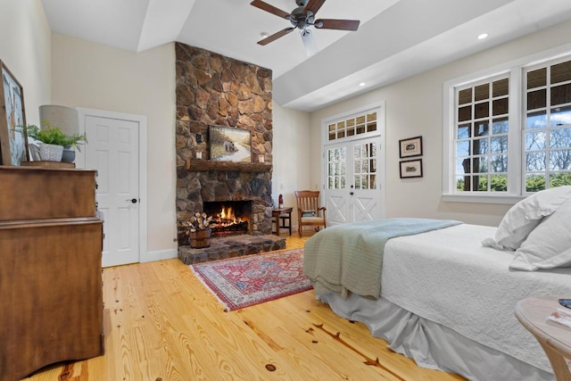 bedroom featuring light wood-type flooring, baseboards, a fireplace, lofted ceiling, and ceiling fan