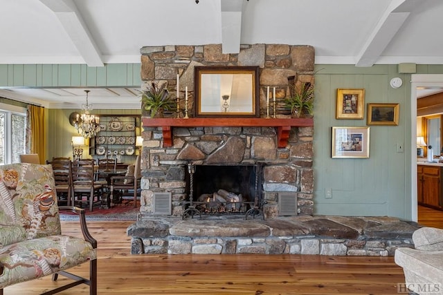 living room featuring hardwood / wood-style flooring, a chandelier, a stone fireplace, and beamed ceiling