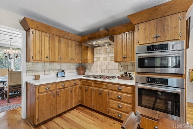 kitchen with backsplash, light hardwood / wood-style flooring, stainless steel appliances, and wall chimney exhaust hood