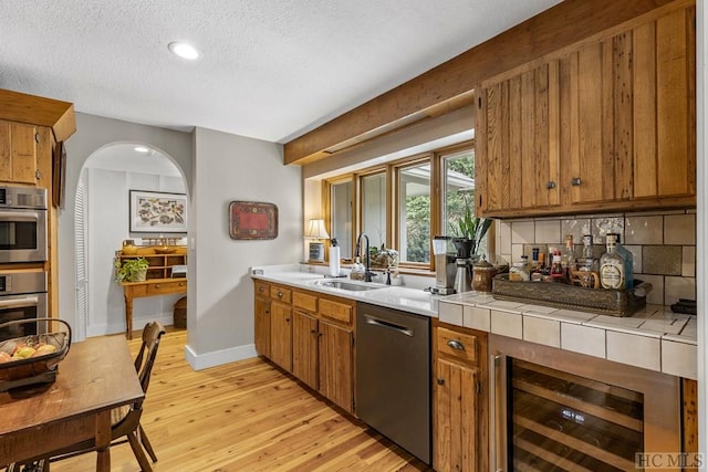 kitchen with beverage cooler, appliances with stainless steel finishes, light hardwood / wood-style floors, sink, and tile countertops