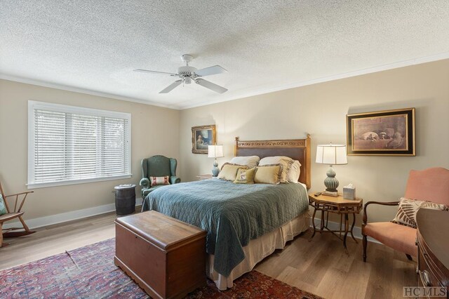 bedroom with ceiling fan, a textured ceiling, ornamental molding, and light wood-type flooring