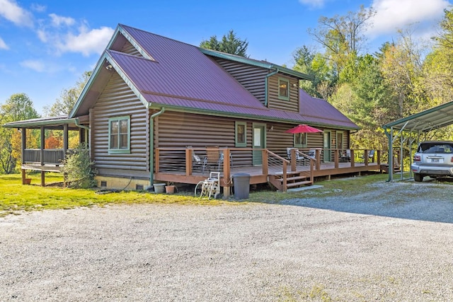 view of front facade with a wooden deck, log exterior, a detached carport, driveway, and metal roof