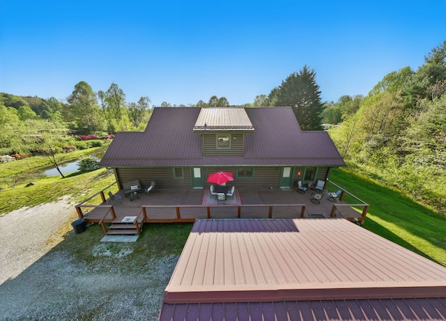rear view of property with a yard, a deck with water view, and metal roof