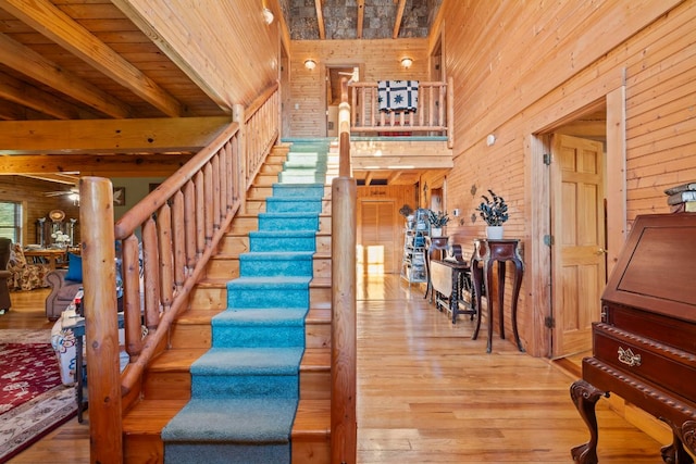 stairway featuring a towering ceiling, wood finished floors, wooden walls, and ceiling fan