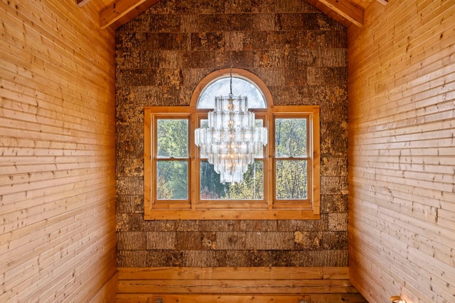 empty room with an inviting chandelier, vaulted ceiling with beams, and a healthy amount of sunlight