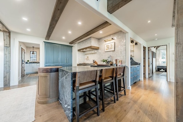 kitchen with a breakfast bar area, light wood-type flooring, backsplash, beamed ceiling, and plenty of natural light