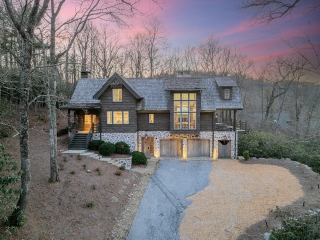 view of front of property featuring an attached garage, driveway, stone siding, stairway, and a chimney