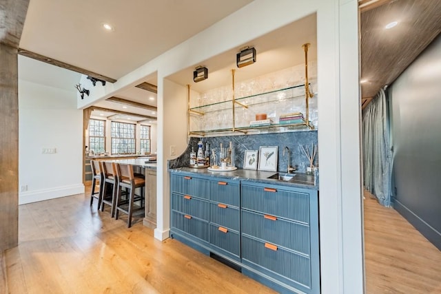 bar featuring light wood finished floors, wet bar, decorative backsplash, and a sink