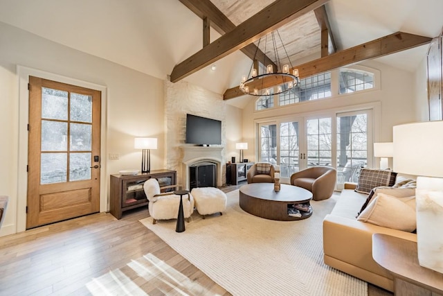 living area featuring a notable chandelier, a fireplace with raised hearth, wood finished floors, high vaulted ceiling, and beamed ceiling