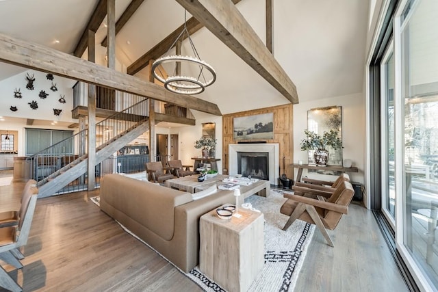 living area with a fireplace with raised hearth, wood finished floors, stairs, beamed ceiling, and an inviting chandelier