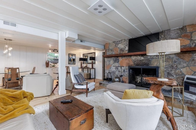 living area featuring a stone fireplace, heating unit, wood finished floors, and visible vents