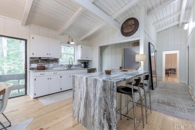 kitchen featuring lofted ceiling with beams, white cabinets, light wood-style flooring, stainless steel refrigerator, and a breakfast bar